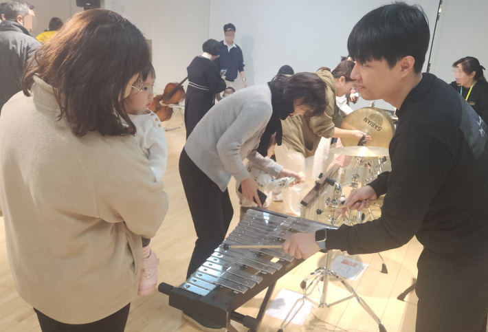 연주자의 안내로 실로폰을 체험하는 아이와 보호자