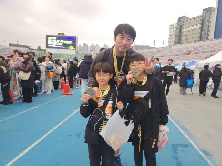 수원종합운동장 결승선 구간에서 완주 메달을 목에 건 참가자 가족이 기념촬영을 하고 있다. 가족과 함께 달린 5km 코스는 특별한 추억으로 남았다.