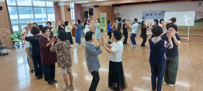수원 곡선동 주민자치센터에서 포즐사 회원들이 포크댄스를 배우고 즐기는 장면