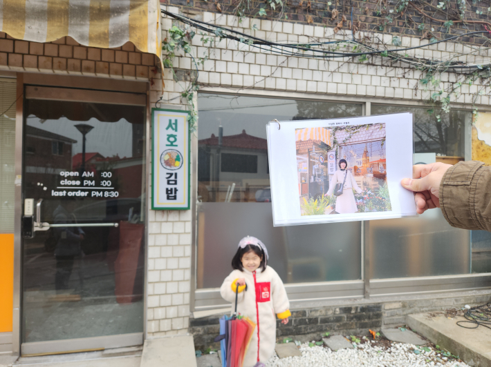 드라마'이상한 변호사 우영우' 촬영지로 알려진 행궁동 김밥집 앞에서 촬영 장면 사진과 같은 구도로 사진을 찍고 있다