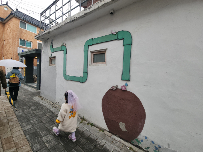 비가 내리던 행궁동 골목에서 아이가 벽화 옆을 따라 걷고 있다. 천천히 걸으며 골목 풍경을 즐길 수 있는 '왕의 골목' 탐방 코스