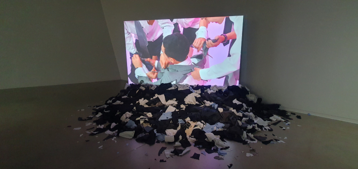 화면 아래에 실제 옷무더기를 쌓아둔 후유히코 타카타 영상 작품 〈컷 슈트(Cut Suits)〉