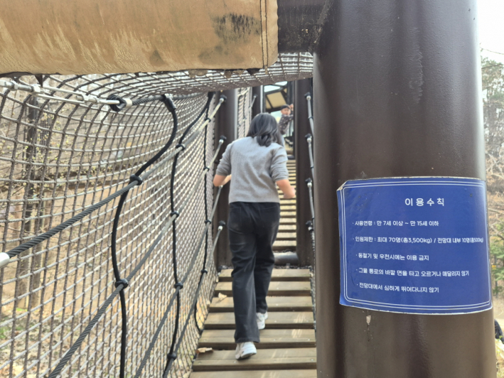 그물 통로를 따라 올라가는 구조물 입구에는 이용 연령과 인원 제한 등 안전 수칙이 함께 안내되어 있다.