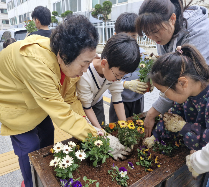 어르신이 아동에게 꽃 심는 방법을 알려주는 모습