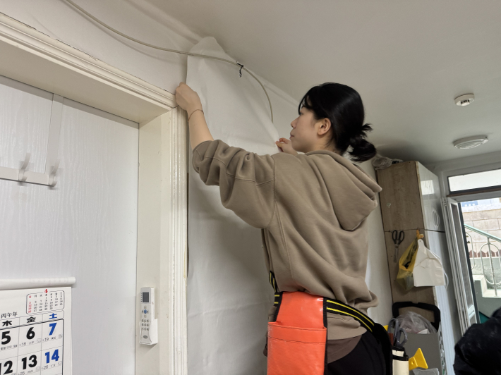 벽에 벽지를 붙이는 대학생의 모습