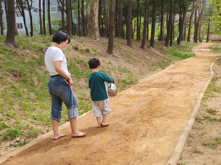부모와 아이가 함께 맨발로 흙길을 걸으며 자연 체험을 하는 모습