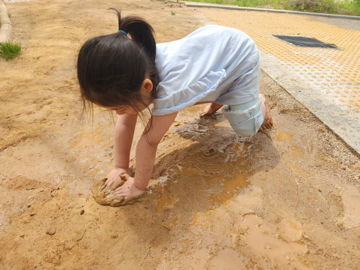 황톳길 위에서 맨발로 흙을 만지며 촉감을 즐기고 있는 아이의 모습