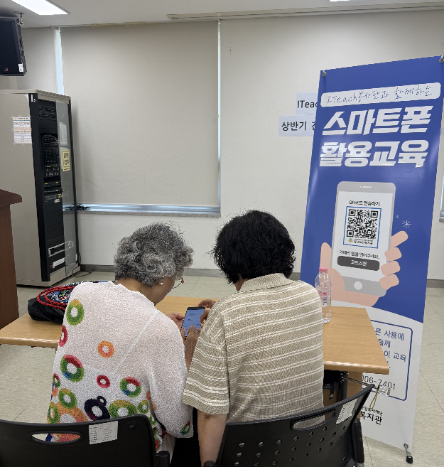 봉사자가 어르신의 스마트폰 사용 과정을 살펴보며 기능을 반복 설명하고 있다.