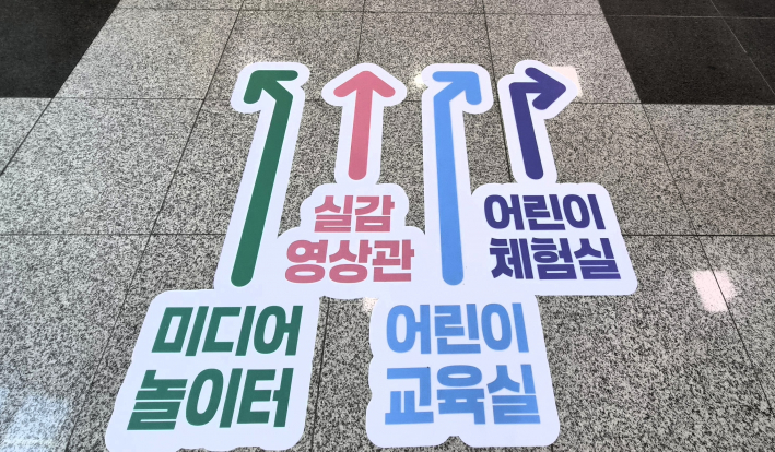 박물관 내부 바닥 안내 사인. '미디어놀이터', '실감영상관', '어린이교육실', '어린이체험실'로 향하는 화살표가 행사장을 찾은 가족들의 발걸음을 안내하고 있다.