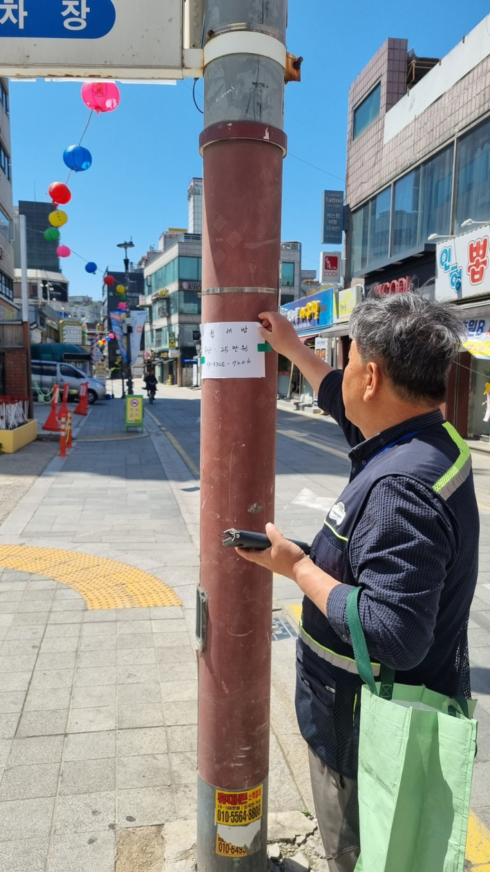 행궁동 경기행복마을관리소 지킴이가 전신주에 부착된 불법 전단지를 떼고 있다.