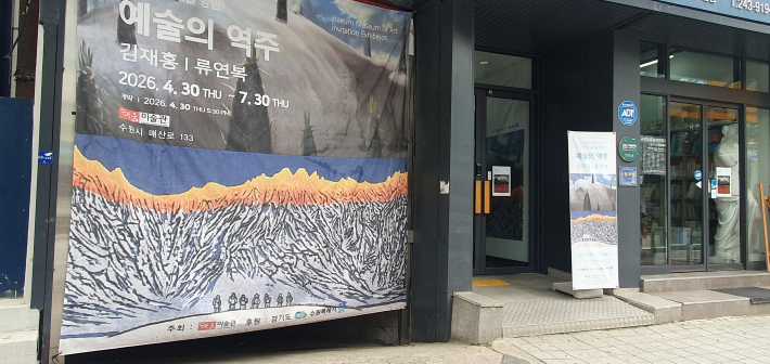 해움미술관 외벽에 걸린 《보편적 실재를 향한 예술의 역주》 대형 현수막과 입구 전경. 수원 도심을 지나던 중 전시를 발견하게 된 장면을 보여준다.