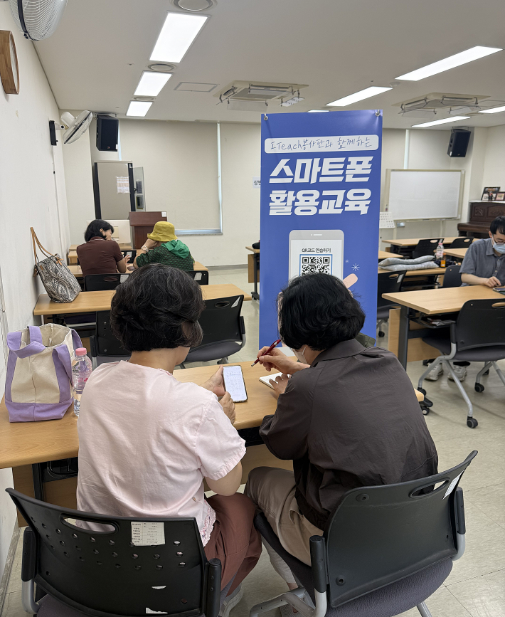 ITeach 봉사자가 어르신과 1대1로 나란히 앉아 스마트폰 활용법을 설명하고 있다.  