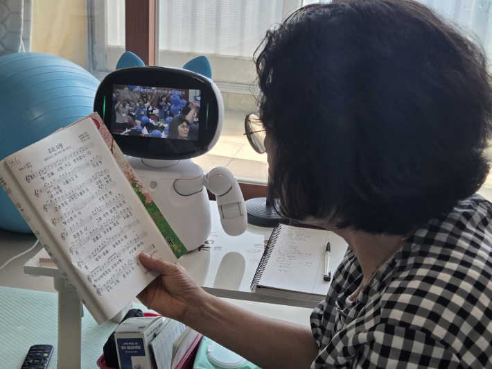 어르신이 AI 돌봄로봇과 함께 노래를 따라 부르며 즐거운 시간을 보내고 있는 모습