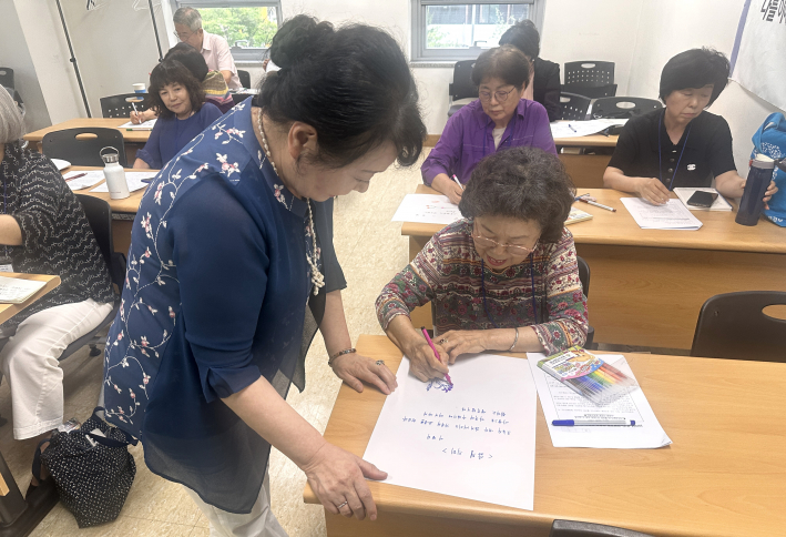 진순분 강사가 직접 글쓰기 및 그림 실습을 하는 수강생의 자리로 찾아가 다정하게 소통하며 문장 작성을 돕고 있다.