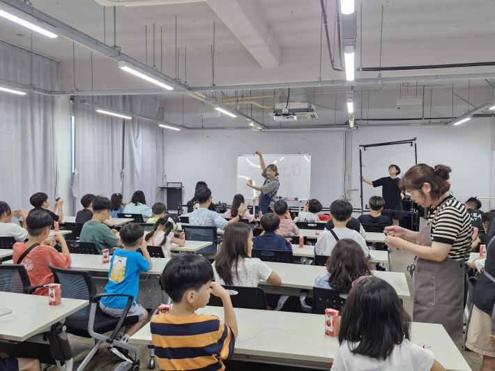 강사가 가죽 지갑 만들기를 아이들 눈높이에 맞게 그림을 곁들여서 설명하고 있다. 