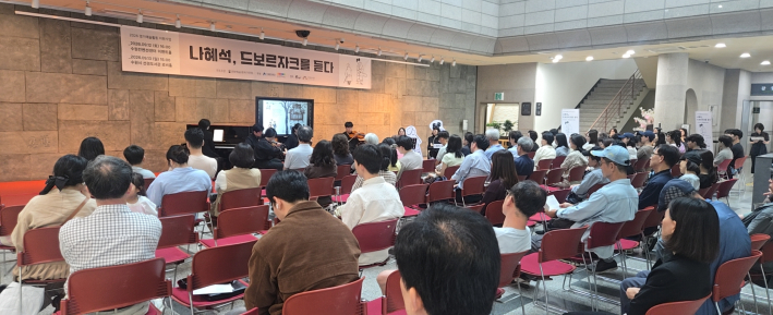 문화예술공동체 더뮤엘의 그림책 클래식 콘서트 나혜석, 드보르자크를 듣다 공연 현장 전경. 로비를 가득 채운 관객들이 연주와 낭독에 귀를 기울이고 있다.
