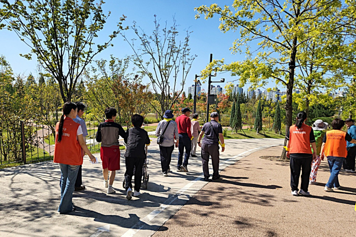 화창한 가을 날씨 속, 조별로 짝을 이룬 어르신들과 봉사자들이 일월수목원의 푸른 숲길을 걸으며 환하게 웃고 있다