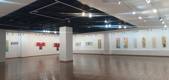 용인문화예술원에서 열린 《결을 잇는 동행》 전시장 전경. 복식 형태의 작품과 다양한 평면 작품이 넓은 벽면을 따라 이어져 있다.