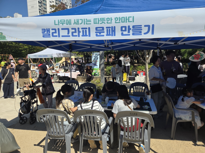 캘리그라피 문패 만들기 체험 부스에서 어린이와 주민들이 정성스레 자신만의 문패를 만들며 즐거운 시간을 보내고 있다.