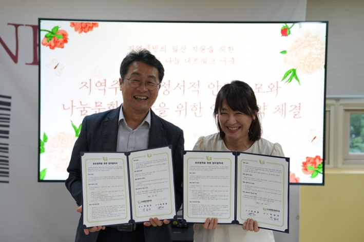 능실종합사회복지관 박일규 관장과 플레리나 대표가 지역주민의 정서적 안정과 나눔문화 확산을 위한 업무협약을 체결한 뒤, 나란히 서서 펼친 협약서를 들고 환하게 웃으며 기념촬영을 하고 있다.
